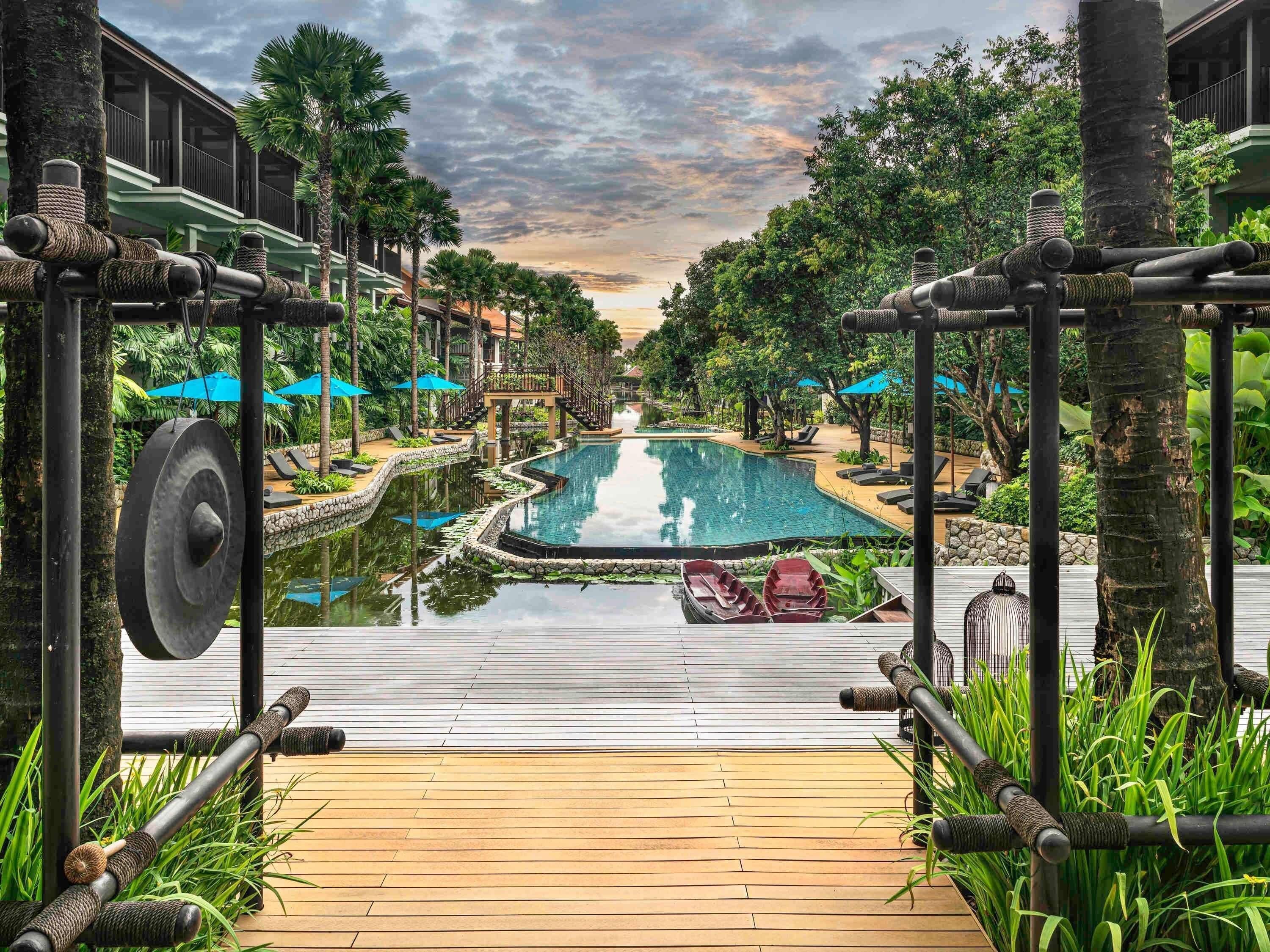 A resort with a pool, wooden deck, and tropical vegetation.