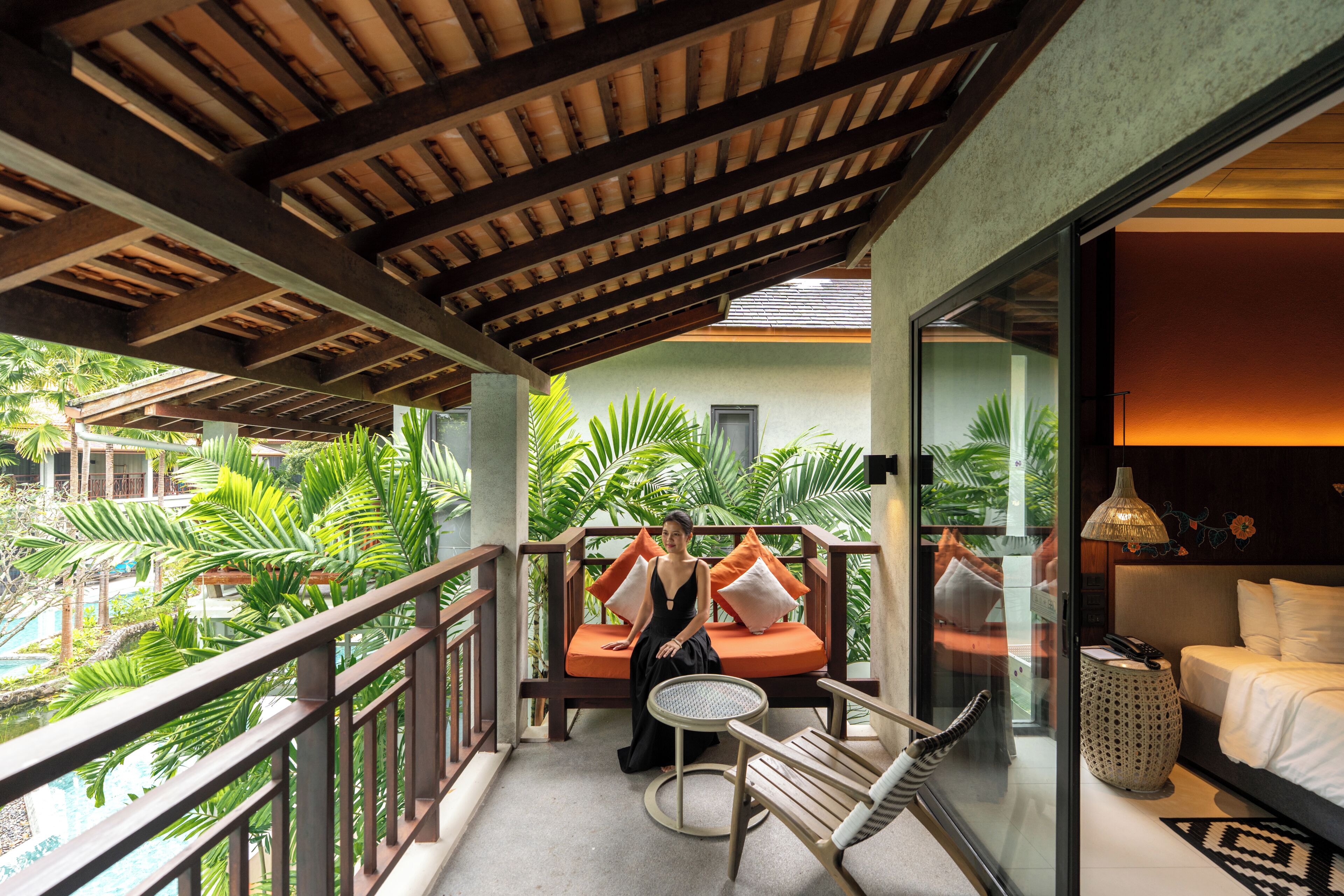 A balcony with a wooden railing, a round table, and a sofa with orange cushions.