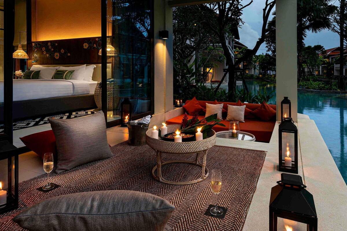 Ein gut beleuchteter Innenbereich mit Sitzgelegenheiten und Blick auf einen Pool, ausgestattet mit einer Couch, einem runden Tisch und Kerzen.