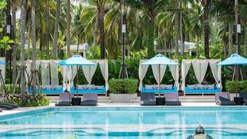 Un área de piscina con toldos azules y blancos, sillones de descanso y una piscina azul cristalina.