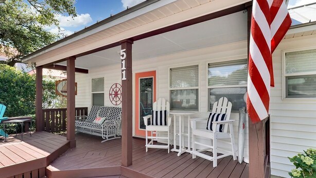 A covered porch with a wooden deck, white chairs, and a small table. - River Hideaway Retreat (Southport)