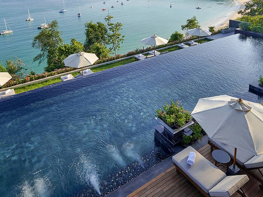 Ein Infinity-Pool auf dem Dach mit Blick auf das Meer und Boote, umgeben von Liegestühlen und Sonnenschirmen.
