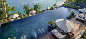 Una piscina infinita en la azotea con vistas al mar y barcos, rodeada de sillones de descanso y sombrillas.