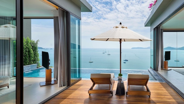A modern balcony with wooden flooring, two lounge chairs, a table with an umbrella, and a glass door leading to a pool. - V Villas Phuket - MGallery (Wichit)