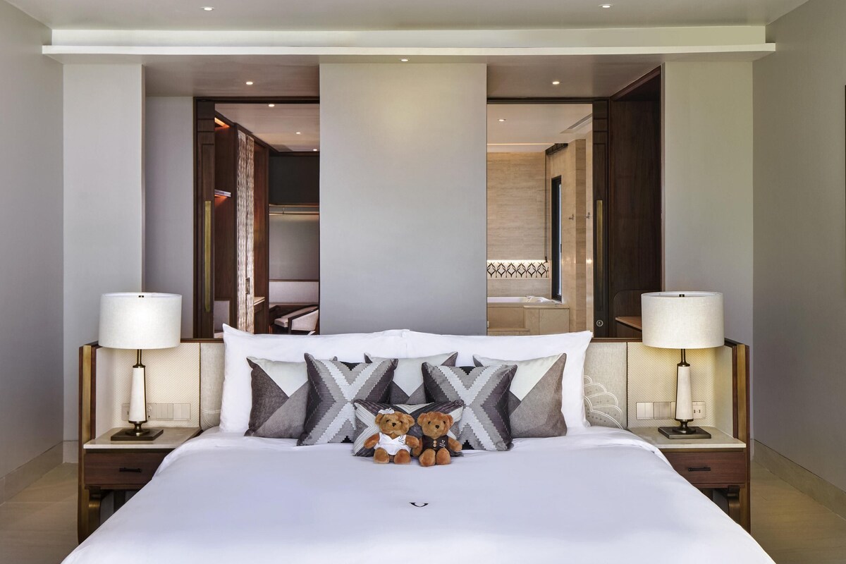 A hotel room with a large bed, two bedside tables with lamps, a mirror, and a view into the bathroom.