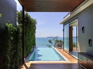 Piscina moderna con vista al mar, terraza de madera y puerta de cristal que da a un balcón.