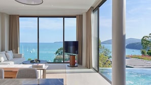 A modern living room with a large window overlooking a coastal view, including a pool and boats. - V Villas Phuket - MGallery (Wichit)