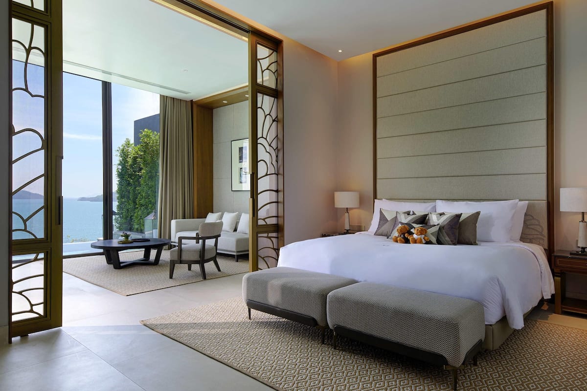 A hotel room with a large bed, a sofa, a dining table, and a view of the sea.