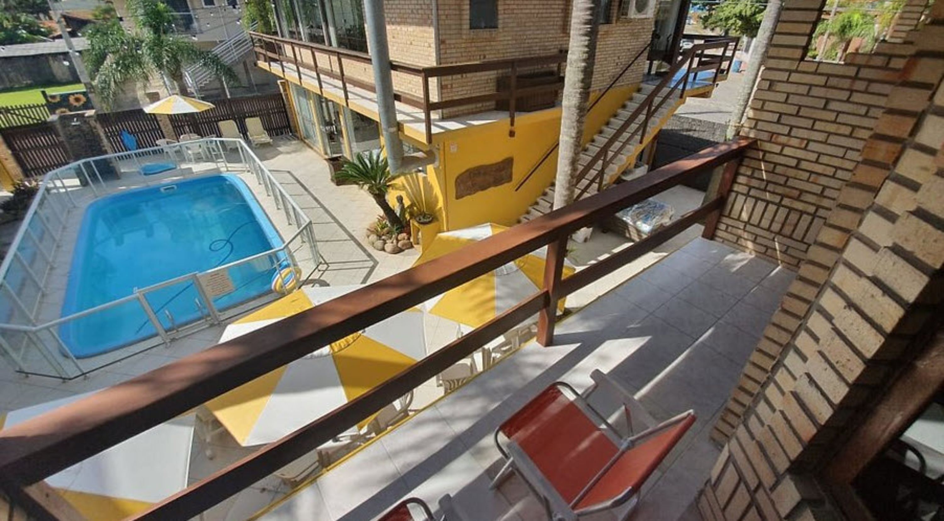 A balcony with a pool, a red chair, and a yellow and white sun lounger.