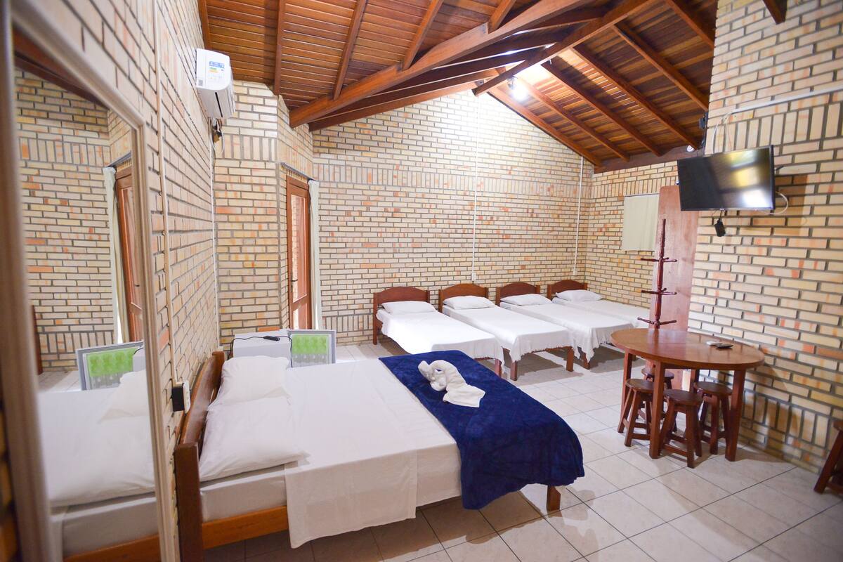 A hotel room with four single beds, a small dining table, and a TV mounted on the wall.