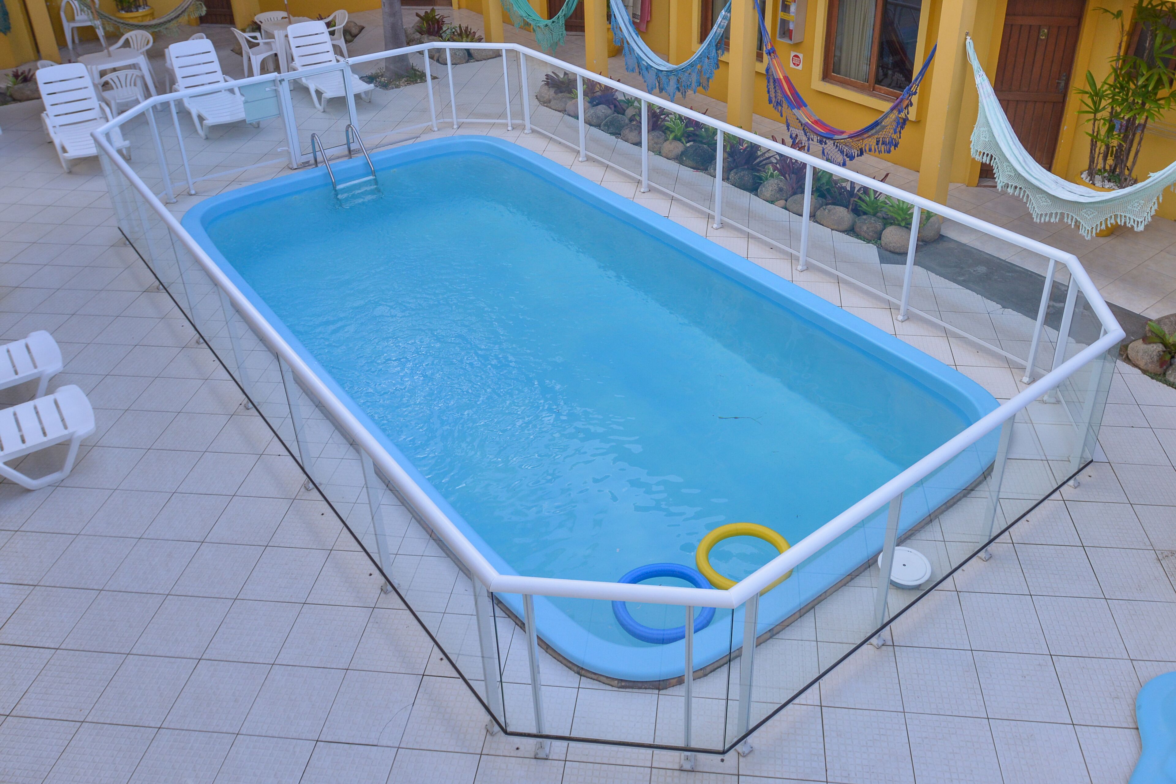 A rectangular pool with a white metal railing, surrounded by white lounge chairs and a hammock.