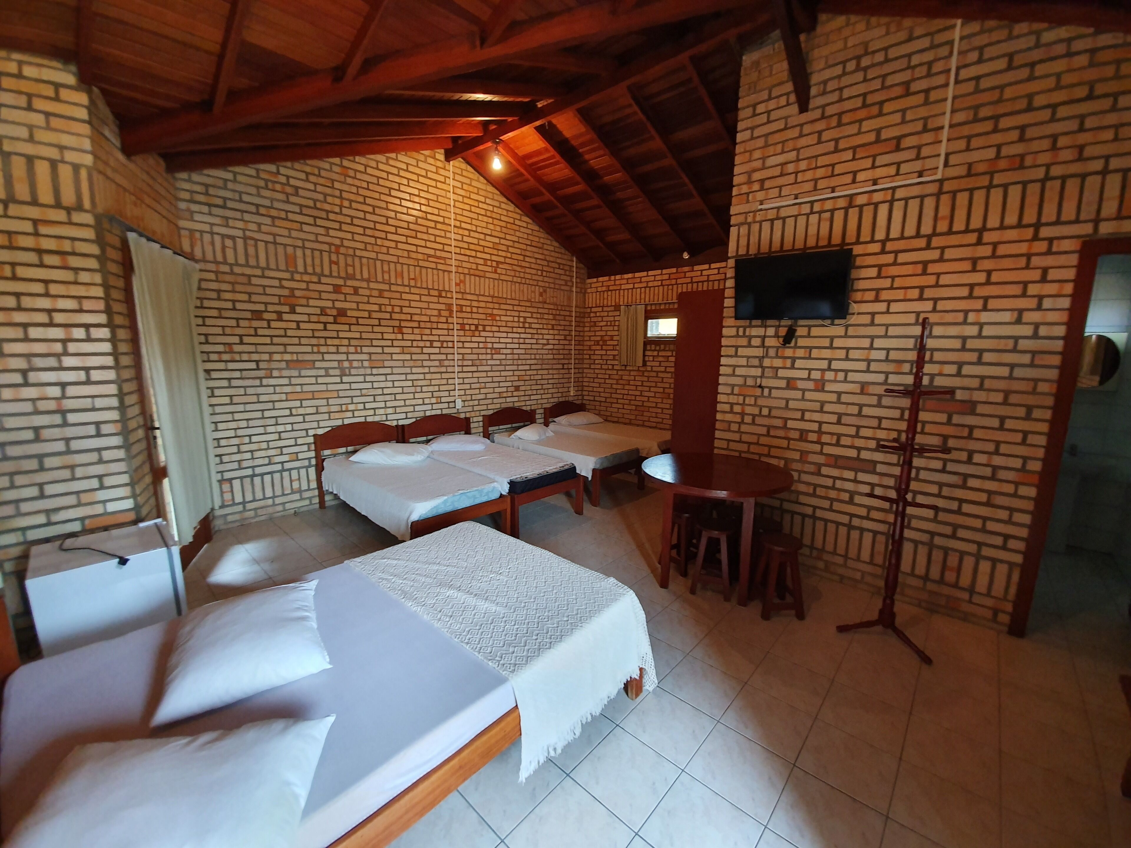 Una habitación con cuatro camas, un televisor instalado en la pared de ladrillo y una pequeña mesa con taburetes.