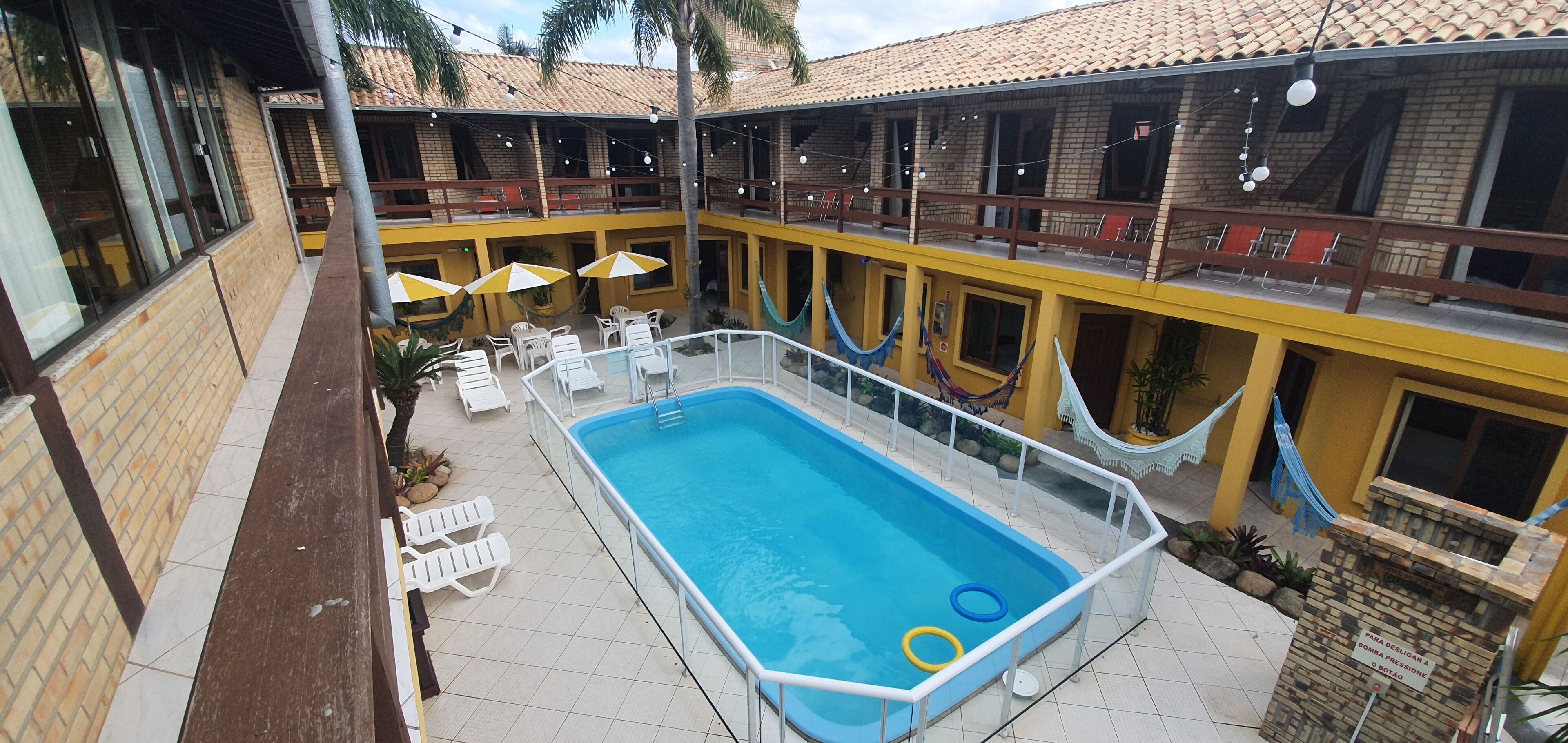 A pool area with lounge chairs and umbrellas, a fenced pool, and a building with multiple balconies.
