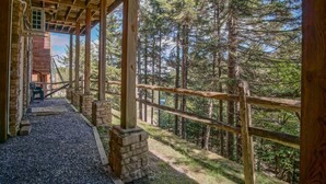 Una terrazza in legno riparata, sostenuta da pilastri in pietra, che conduce a una zona boschiva.