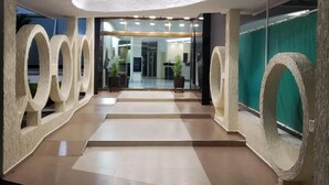 Un hall d’hôtel moderne avec un escalier central, de grandes colonnes circulaires et une entrée en verre.