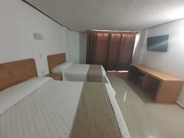 A hotel room with two beds, a desk, and a TV mounted on the wall.