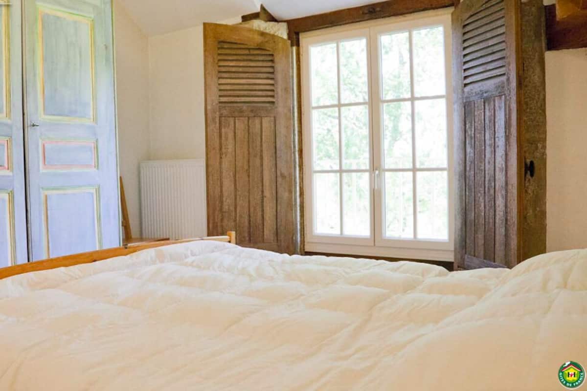 Een slaapkamer met een groot bed, houten deuren en een raam met luiken.