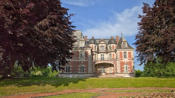 Een groot, historisch gebouw met een symmetrische gevel, meerdere schoorstenen en een centrale ingang met een portico.