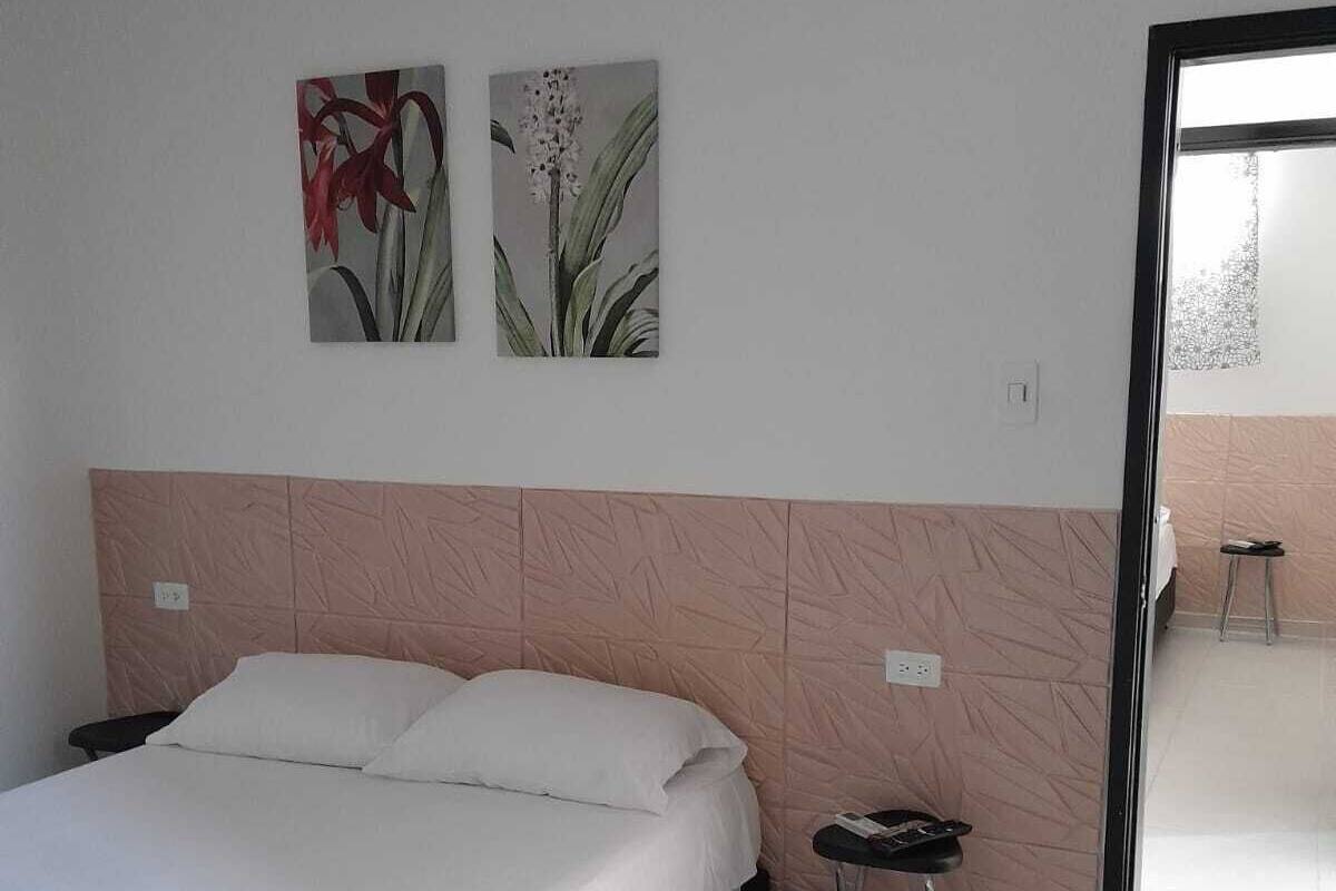 A bedroom with a bed, a nightstand, a small stool, and two wall-mounted paintings.