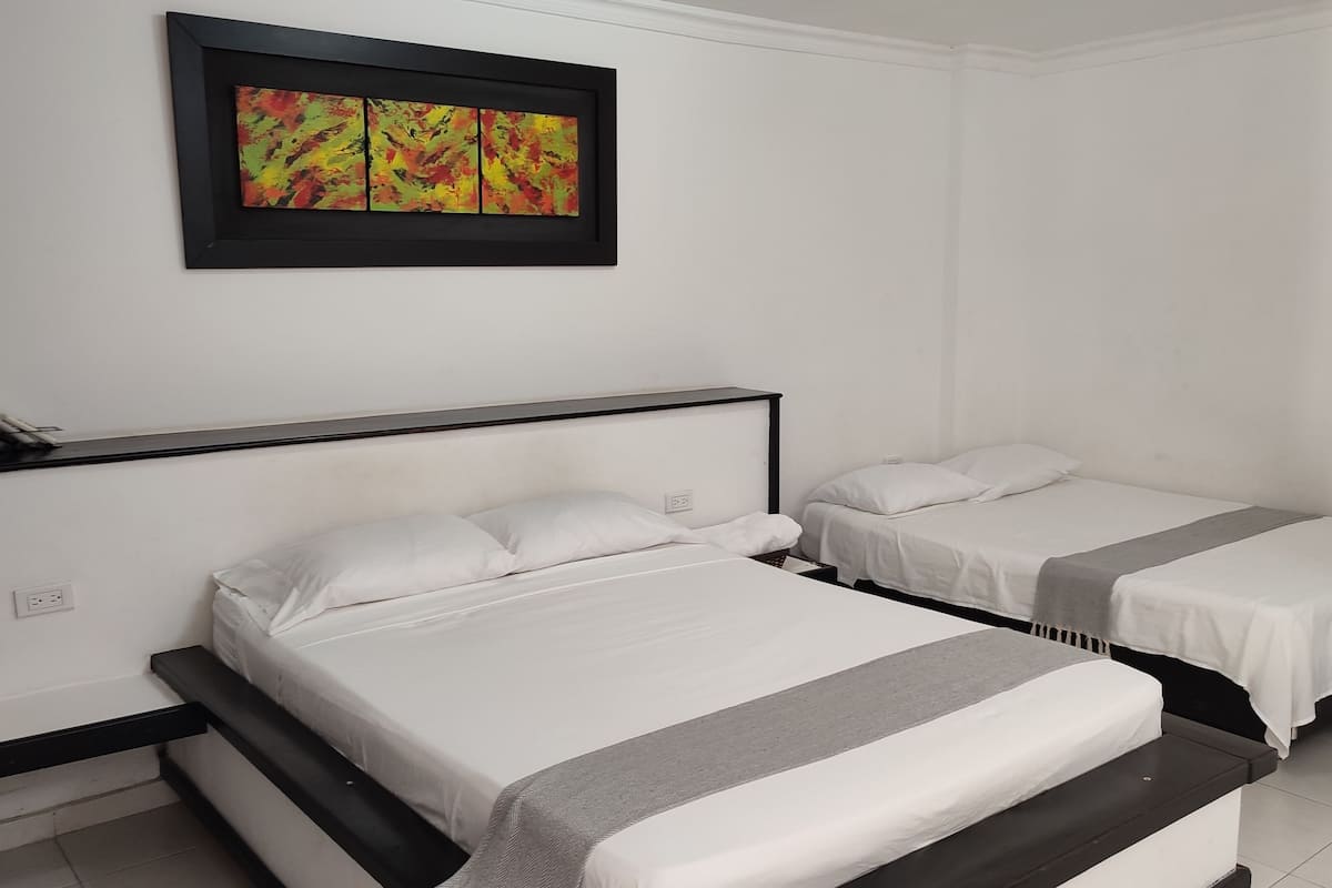 A hotel room with two beds, a black headboard, a gray blanket, and a colorful abstract painting on the wall.
