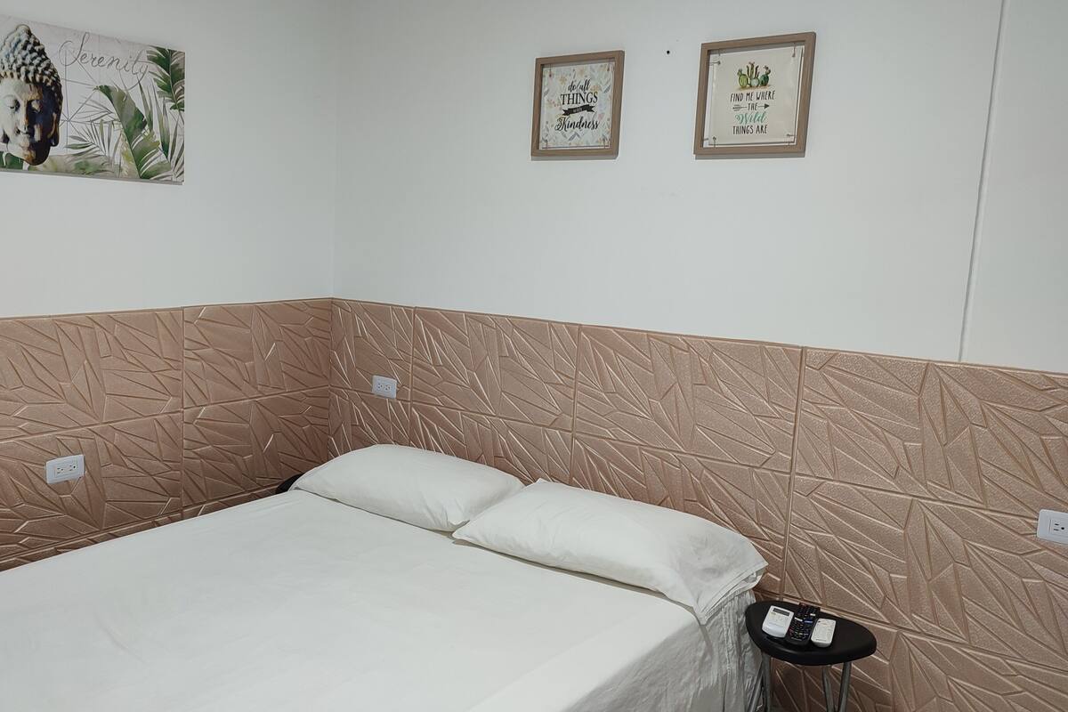A bedroom with a bed, two wall-mounted pictures, and a wall with a geometric pattern.