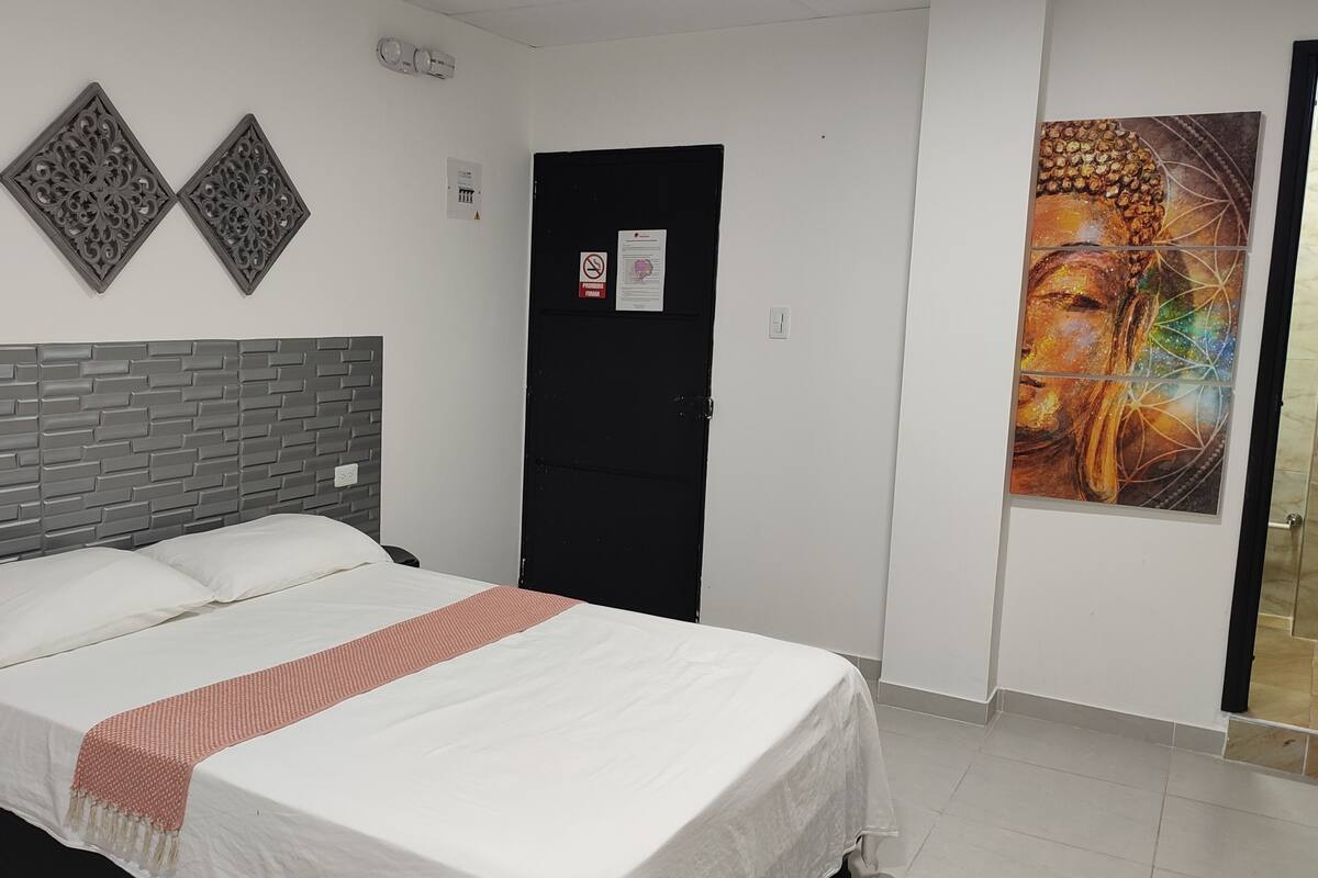 A bedroom with a brick-patterned headboard, a bed with white linens, a red throw blanket, and a large Buddha painting on the wall.