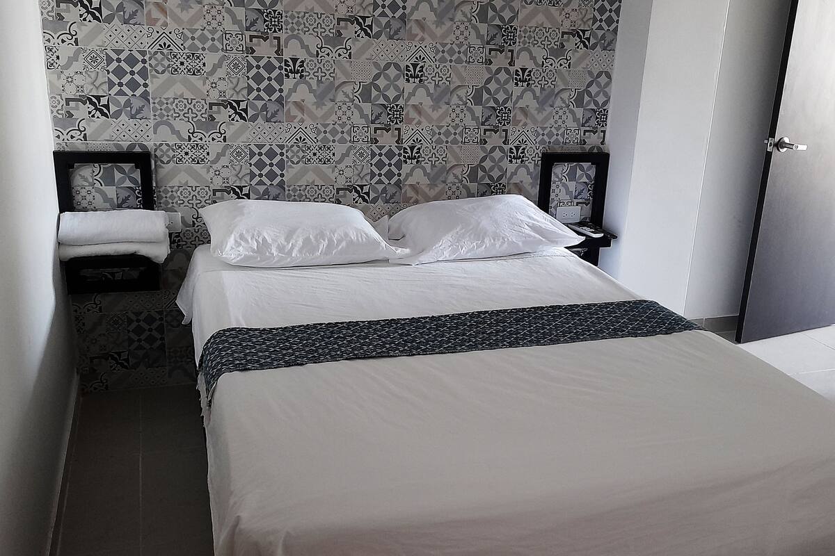A neatly made bed with white linens, a patterned wall, and a door to the right.