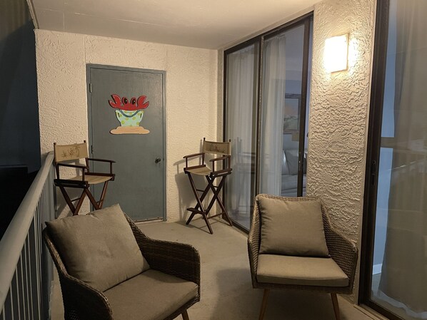 Um quarto com duas cadeiras de vime, uma porta com adesivo floral e uma janela grande com cortinas.