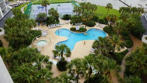 Een resort met een groot zwembad, tennisbanen en palmbomen.