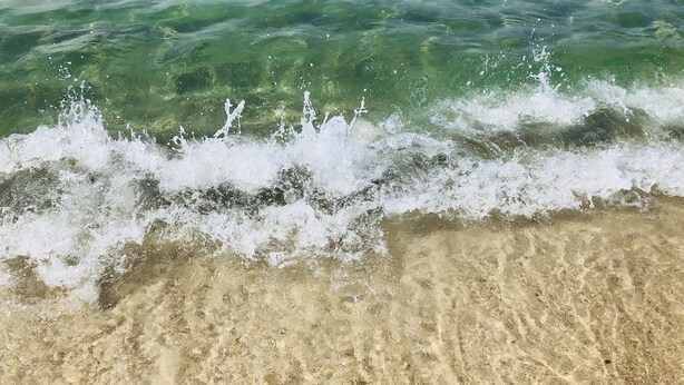 Een zandstrand met helder water en golven.