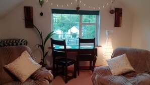 Ein gemütliches Zimmer mit zwei Sesseln, einem Esstisch und einem großen Fenster mit Blick auf ein Haus und Bäume.