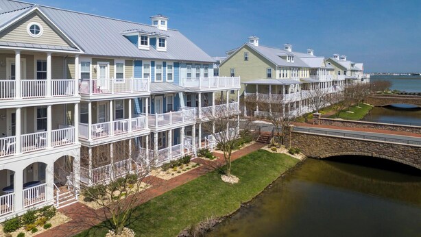 A row of multi-story waterfront properties with balconies, a stone bridge, and a river. - Amazing 4 Bedroom Sunset Island Townhome with Bonus Den! (Ocean City)