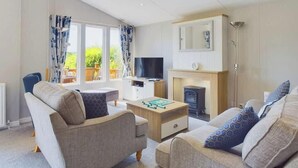 Ein Wohnzimmer mit Sofa, Sessel, Fernseher, Kamin und einem Fenster mit Vorhängen.
