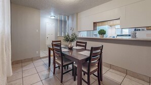 Un comedor con una mesa y sillas de madera, un jarrón con flores, y una cocina al fondo.