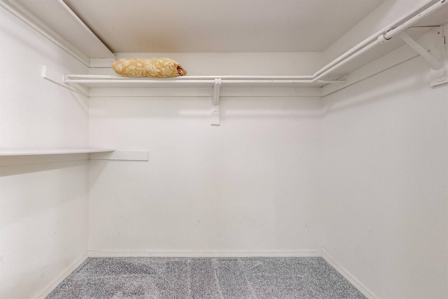 A corner of a room with a white ceiling, a grey speckled floor, and a beige patterned pillow on a white shelf.