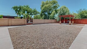 Un patio cubierto con suelo de grava, una pérgola roja y una pared de ladrillo.