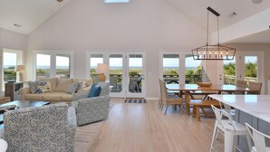 A spacious living area with a high ceiling, large windows, and a view of the ocean. - "Love At First Sight" - Oceanfront Home w/ Private Pool, 7 Bedrooms / 5.5 Bathrooms (Holden Beach)