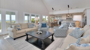 A spacious living room with a high ceiling, large windows, and a view of the outdoors. - "Love At First Sight" - Oceanfront Home w/ Private Pool, 7 Bedrooms / 5.5 Bathrooms (Holden Beach)
