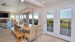 A spacious room with a wooden dining table, wicker chairs, a TV, and a balcony with a view of the beach. - "Love At First Sight" - Oceanfront Home w/ Private Pool, 7 Bedrooms / 5.5 Bathrooms (Holden Beach)