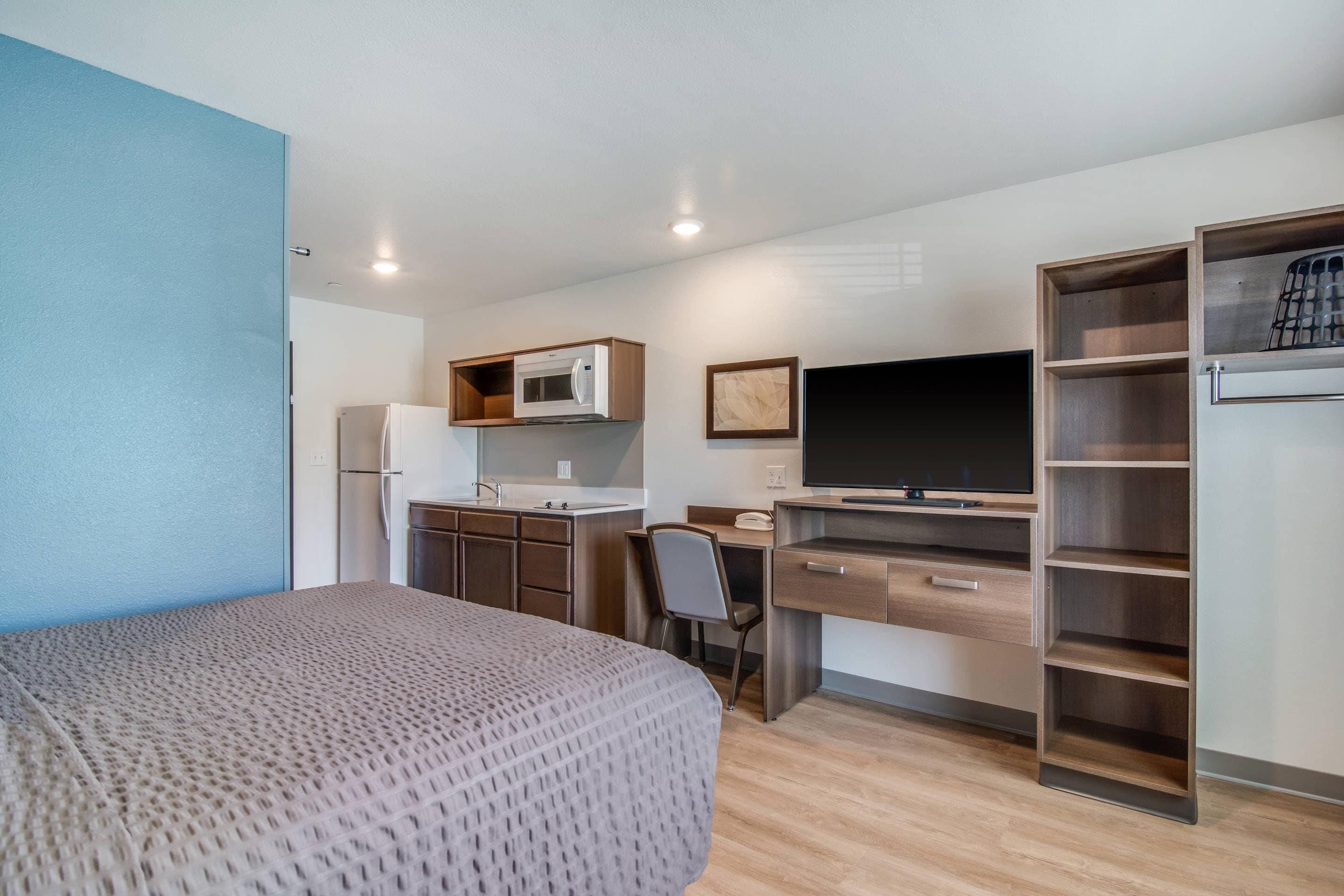 A hotel room with a bed, kitchenette, desk, TV, and wardrobe.