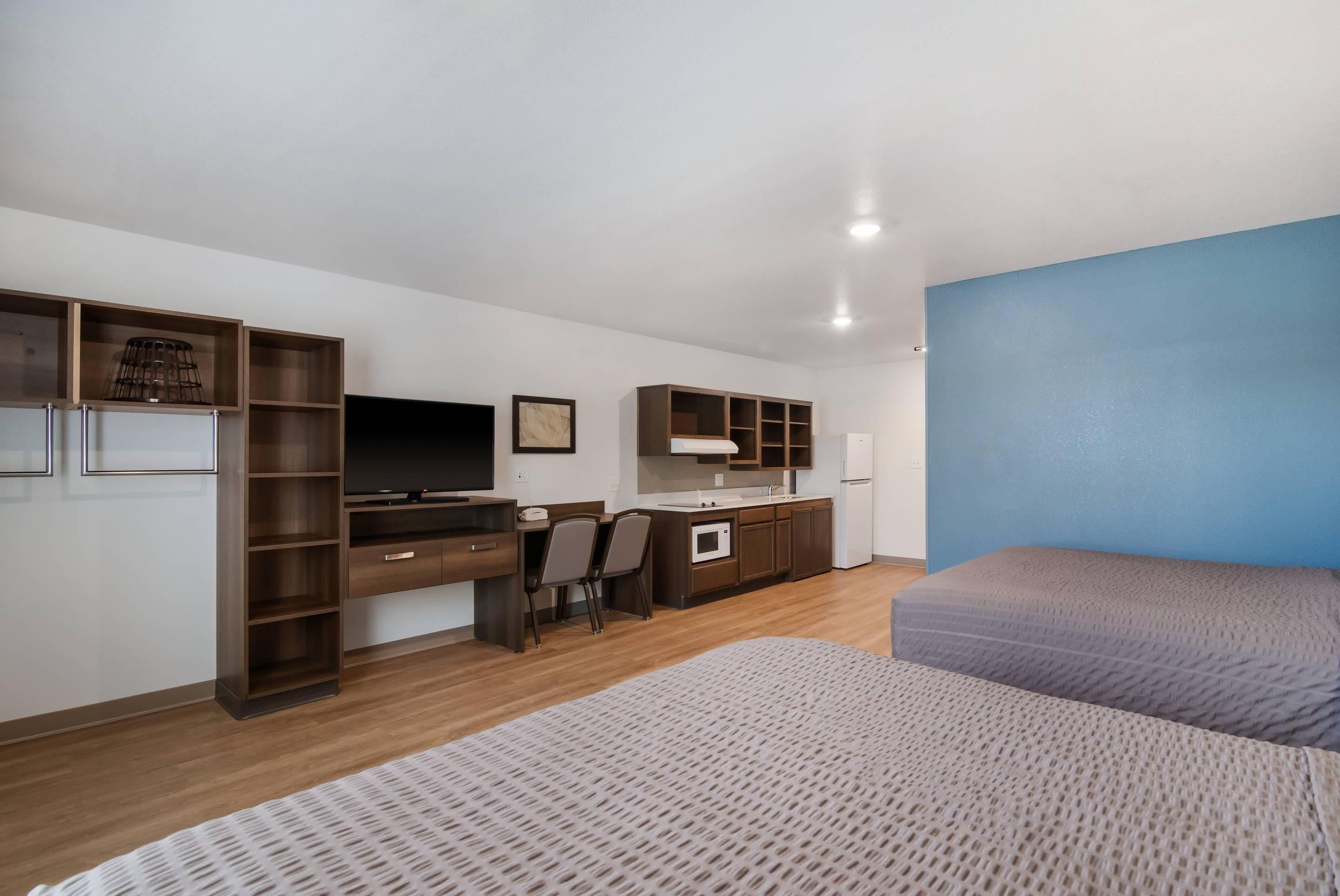 Habitación de hotel con cama, escritorio con ordenador, televisión, kitchenette y una pared de acento azul.