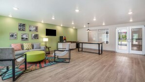 A modern living room with a green wall, a sofa, a coffee table, and a TV mounted on the wall. - WoodSpring Suites Fort Mill (Fort Mill)