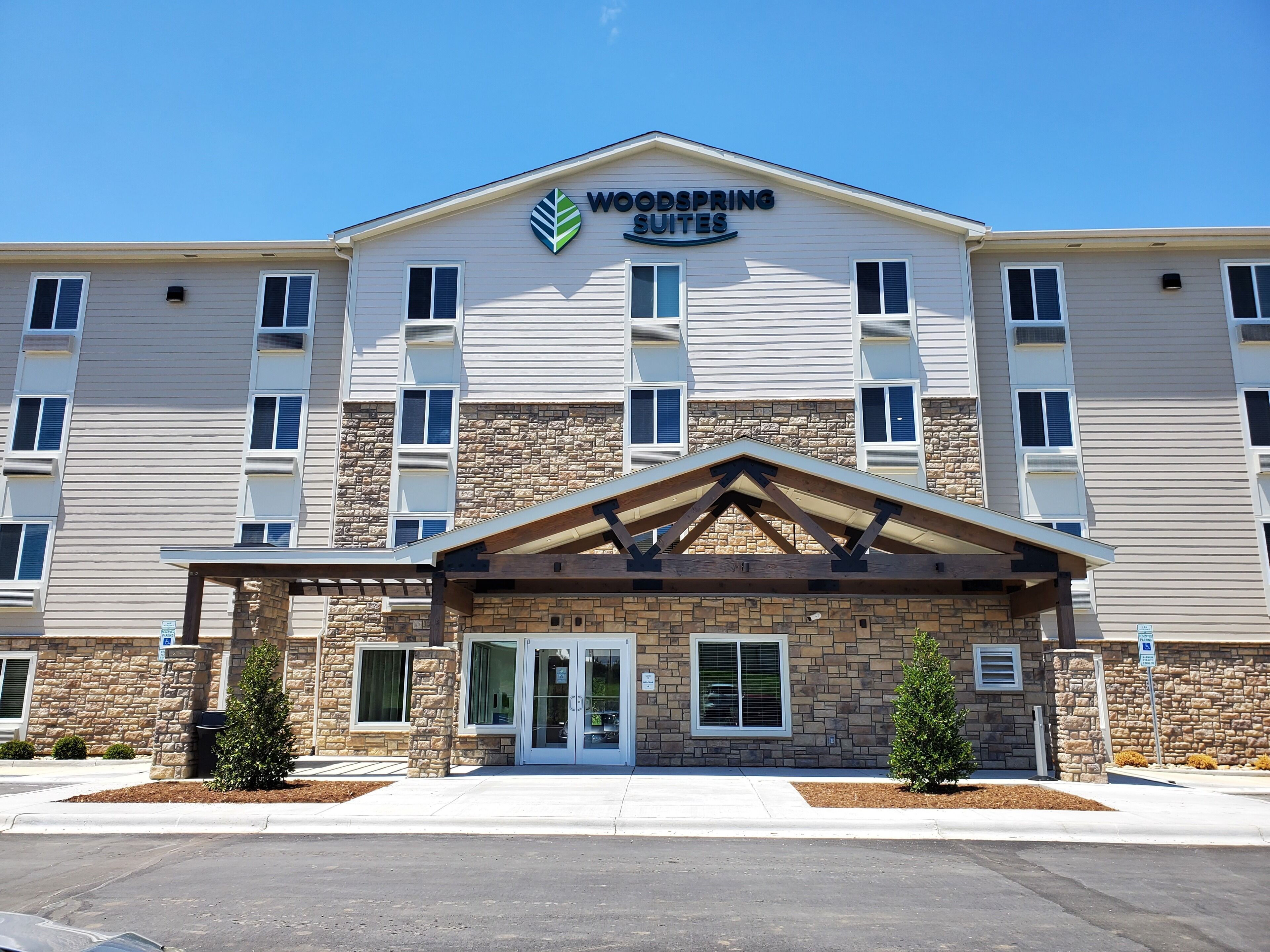 Un hôtel Woodspring Suites doté d’une façade en pierre, de nombreuses fenêtres et d’une entrée abritée.