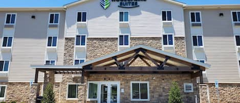 Un hôtel Woodspring Suites doté d’une façade en pierre, de nombreuses fenêtres et d’une entrée abritée.