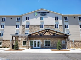 Un hotel Woodspring Suites con fachada de piedra, varias ventanas y una entrada cubierta.