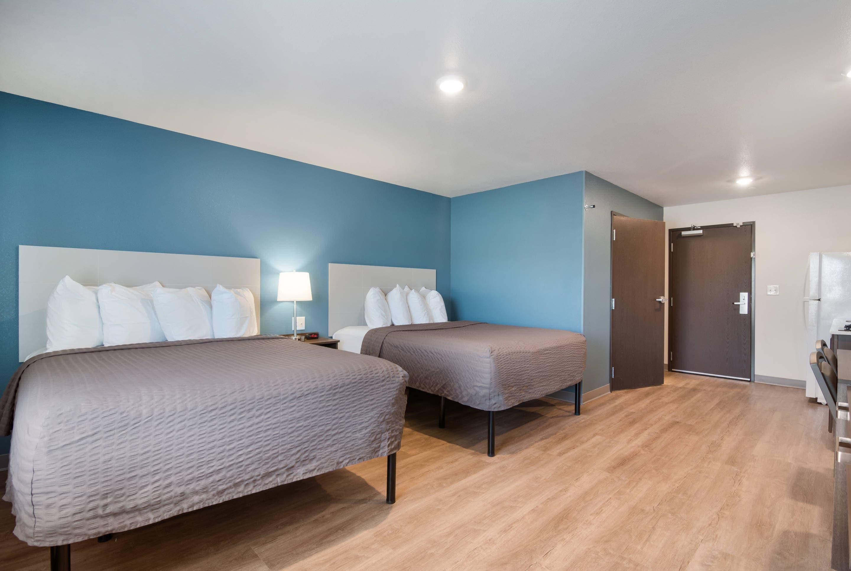 Une chambre d’hôtel avec deux lits, une table de chevet, une lampe, une porte et une petite table avec une chaise.
