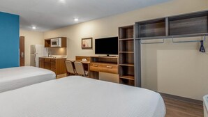 Une chambre d’hôtel avec deux lits, une kitchenette, un bureau avec un ordinateur, une télévision et une armoire.