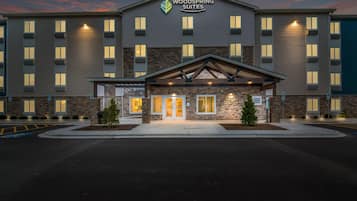 A multi-story hotel with a prominent 'Woodspring Suites' sign, featuring a stone facade and a covered entrance with a pitched roof.