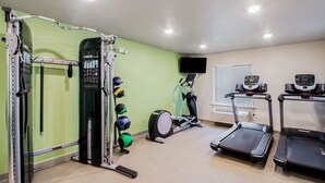 Une salle de sport à domicile équipée d’un support à squats, de balles lestées, d’un vélo elliptique et de tapis de course.