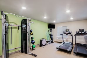 Una palestra in casa con una rack per squat, palle mediche, una ellittica e tapis roulant.